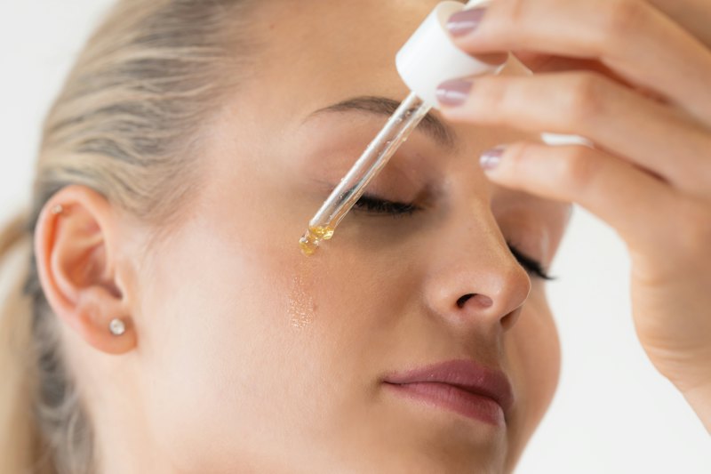 A woman applying a drop of facial serum from a glass dropper